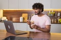 A mestizo young man stands sideways in the kitchen in subdued lighting, holds a bowl of pasta in hands and wraps them in