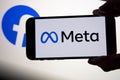META company logo seen on smartphone with Facebook logo on background screen.