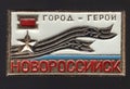 Metal badge with an image of peakless cap, Gold Star and the inscription in Russian `Novorossiysk hero city`
