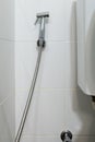 The metal bidet spray is hanging on the white tile wall near the flush toilet Royalty Free Stock Photo