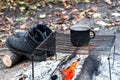 Metal black sooty mug on the grill on an open fire on the background of Hiking boots and autumn leaves. Background.