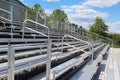 Empty metal bleachers during a sunny spring day with green trees and a blue sky in the background