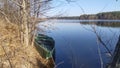 A metal boat with a wooden floor and benches is moored to the grassy shore under the branches of trees. In early spring the river Royalty Free Stock Photo