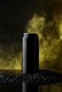 Metal bottle of beer in black sand in smoke and steam. Bright background.