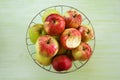 Metal bowl with green, yellow and red apples and one bitten apple on the green wooden background. Royalty Free Stock Photo