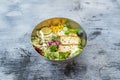 Metal bowl of vegan salad with filleted tofu, sesame seeds, assorted lettuce, sweet corn, sunflower seeds,