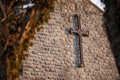 Metal catholic cross on a stone wall, framed by dark trees branches out of focus. Concept catholic faith symbol and religion