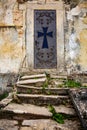 A metal closed door with a cross and an ornament on it and the old dilapidated stairs leading to it. Old building, peeling wall. Royalty Free Stock Photo