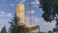 A metal crane is used in the construction of a high-rise concrete apartment building with balconies. There are trees growing next Royalty Free Stock Photo