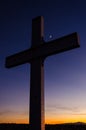 A metal cross under a beautiful, colorful sunset sky and a crescent moon at dusk