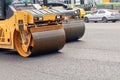 Road rollers compacting fresh asphalt on the carriageway against the backdrop of a city street