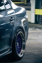 Wet silver shining car body and blue purple metal wheels parked in a parking garage