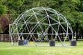 Metal dome like frame with entrance and barrel weights left in local park after concert surrounded with uncut grass and dense