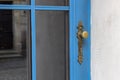 Metal door handle on a beautiful blue wooden door. The window reflects the street of the old town. Royalty Free Stock Photo