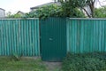 Metal door and wooden fence of planks overgrown with green vegetation Royalty Free Stock Photo