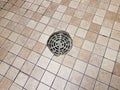 Metal drain and tan and brown square bathroom tiles or floor Royalty Free Stock Photo