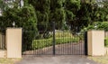 Metal driveway entrance gates set in brick fence with garden trees in background