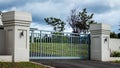 Metal driveway private residence property entrance gates set in brick fence with garden trees in background