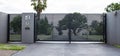 Metal driveway property entrance gates set in concrete fence with garden trees in background