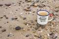 A metal enameled travel mug with pure natural drinking Baikal water on the rocks and sand of the shore of Lake Baikal.