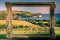 Metal frame opening to New Zealand iconic landscape - lush green hills and cliff over blue sea.