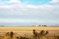 Metal grain elevators on the horizon viewed across harvested wheat field with fence in foreground under big sky