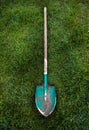 Metal green shovel with wooden handle on grass lawn