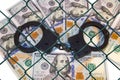 Metal handcuffs on the background of dollars under wire netting (lattice)