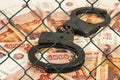 Metal handcuffs on the background of Russian rubles under wire netting (lattice)