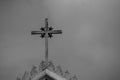 Metal holy cross or crucifix on the top of white church with blue sky in the background.