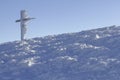 Iron frozen cross, completely covered by snow and icicles and mountain winter landscape under blue sky