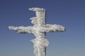 Iron frozen cross, completely covered by snow and icicles and mountain winter landscape under blue sky