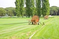 Metal irrigator in a green mowed lawn. Field with green grass and trees