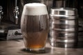 metal keg with foamy wave of beer and glass with frothy head in the background