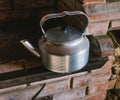 A metal kettle on a red brick stove. Royalty Free Stock Photo