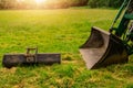 Metal ladle on the grass and one on a green tractor.. Heavy machinery concept. Sun flare in the background. Selective focus