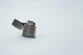 A metal lighter standing in the snow on a light background. Space for text. Royalty Free Stock Photo
