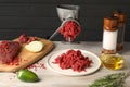 Metal meat grinder with minced beef and products on light wooden table