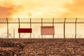 Metal mesh wall with barbed wires security fence and danger notice board on sunset