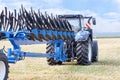 A metal multirow plow is attached to a tractor standing on an agricultural field