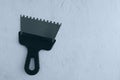 Metal notched construction spatula for tile adhesive with black handle on gray concrete background. View from above