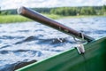 Metal oarlock holding an oar in a boat, against the background of a lake on a summer day.