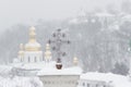 Metal Orthodox cross on the background of winter storm. Snow covered cupola of Lavra in Kiev. Ukrainian landmark.