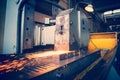 Metal parts on a flat grinder are treated with an abrasive wheel, sparks fly from under the circle, wide-angle photos. Toned photo