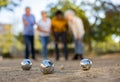 Metal petanque balls against four blurred multiracial senior players in the distance outdoors Royalty Free Stock Photo