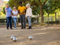 Metal petanque balls against four blurred multiracial senior players in the distance outdoors Royalty Free Stock Photo