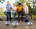 Metal petanque balls against four blurred multiracial senior players in the distance outdoors Royalty Free Stock Photo