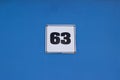 Metal plate with house number 63 black color on white. On a blue wall. The wall of the house Royalty Free Stock Photo