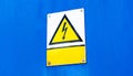 Metal plate sign with a worn yellow high voltage warning triangle symbol and an empty blank text box, blue background, copy space