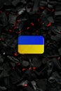 Metal rectangular box with the Ukrainian flag on a charcoal back. Copy space in a rectangle on a background of hot coals